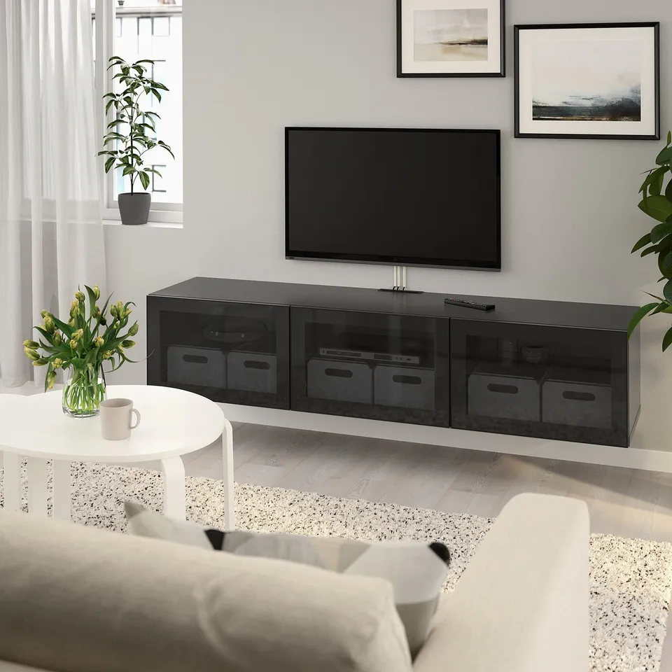 Modern living room with BESTÅ black tv bench, large tv, glass doors, storage, framed wall, white coffee table, flowers, couch, large window, plant.