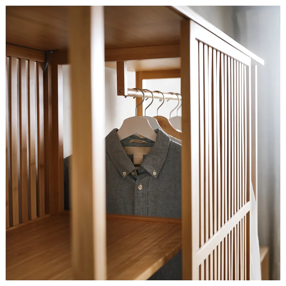A NORDKISA wardrobe in natural bamboo. It sliding doors and hanging space where a grey shirt is visible. The design is minimalistic with clean lines.