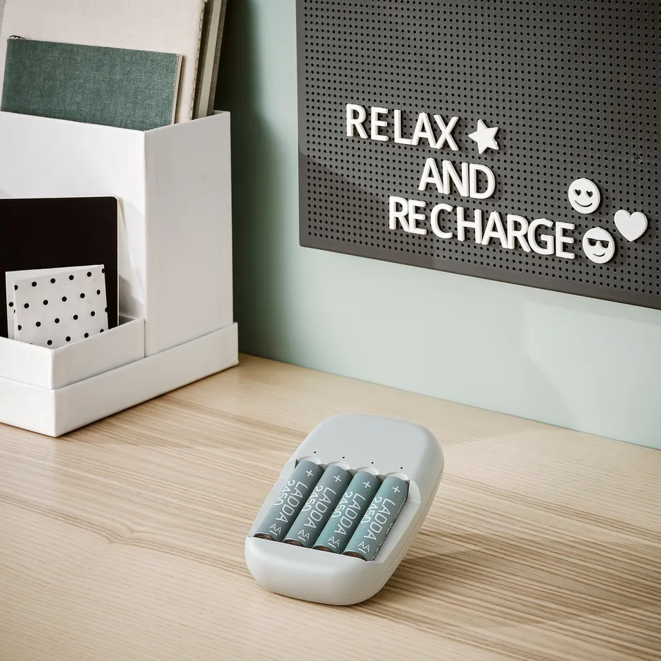 White STENKOL battery charger with 4 ladda grey rechargeable batteries on light wood desk. Small, portable.