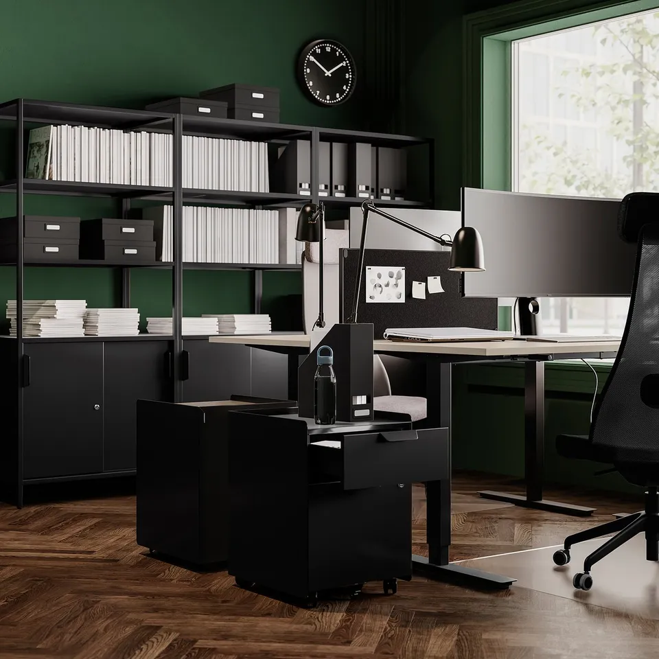 Modern office setup with green walls, wooden floor, black furniture including a desk, chair, file cabinets, and shelves.