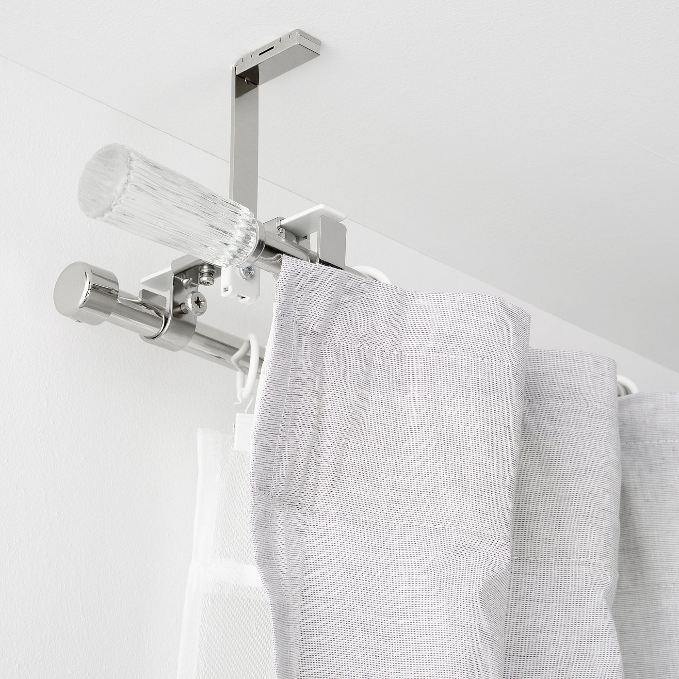 Image shows a mounted double curtain rod set with a glass finial on wall, holding light grey curtains.