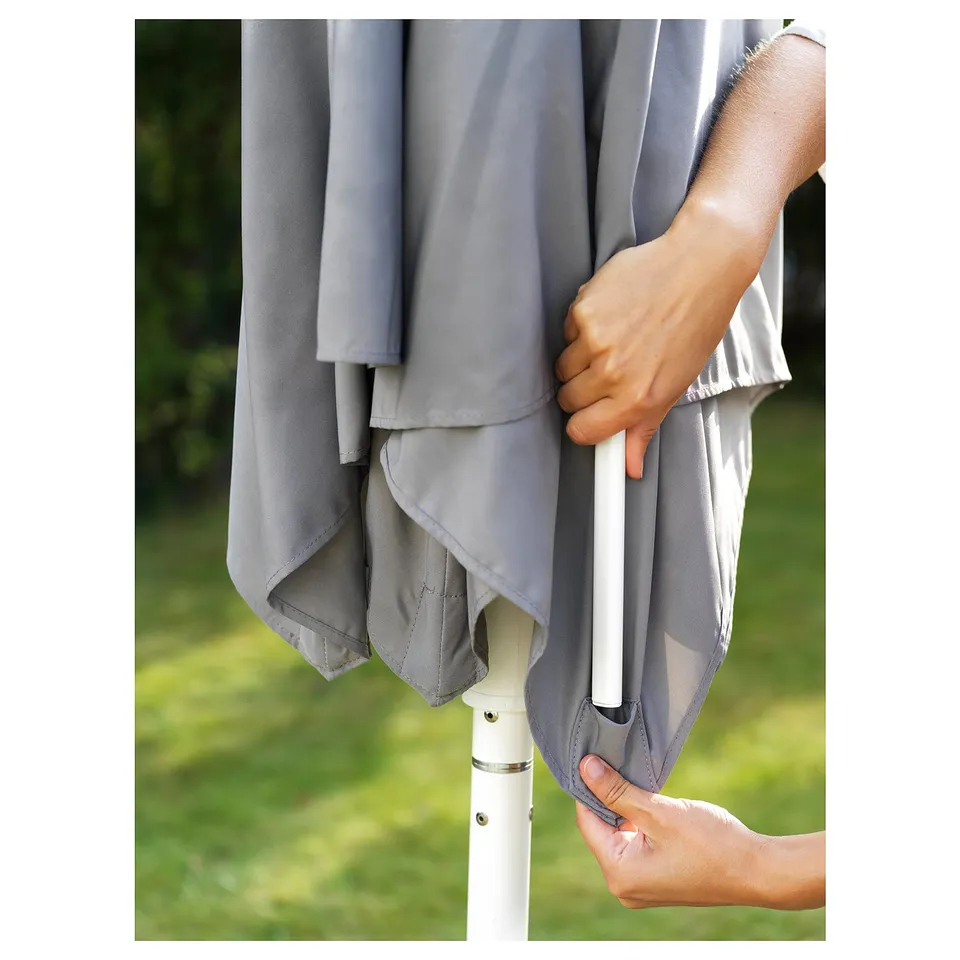 Person adjusting light grey fabric on white parasol pole outdoors.