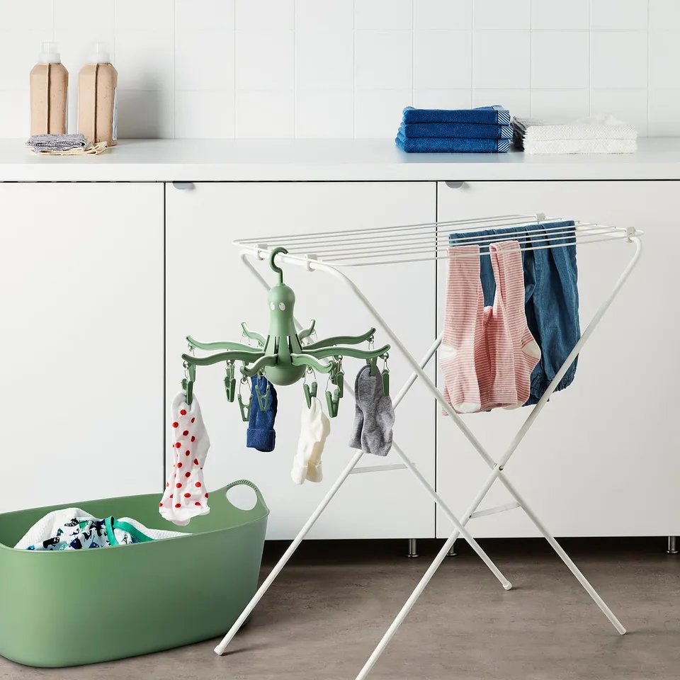 Green PRESSA dryer indoors with clothes, near cabinet & basket.