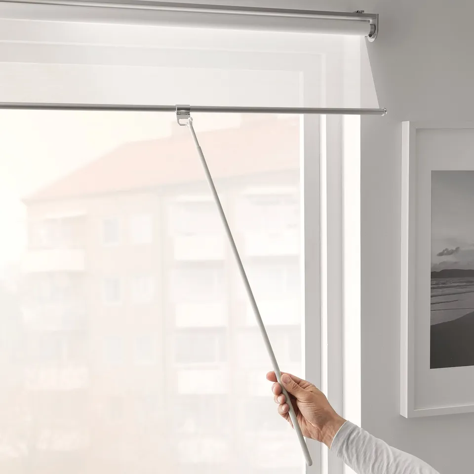 Pulling white roller blind with extendable draw rod on window.