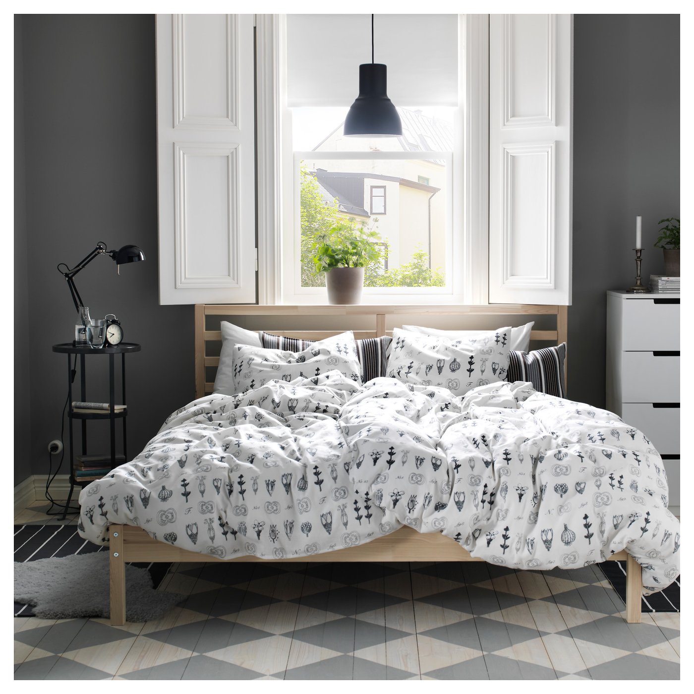 Modern bedroom with TARVA bed, black floral bedding, grey walls, and large window view.