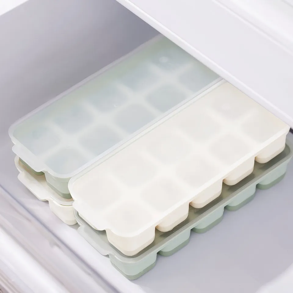 Ice cube trays with lids sit inside a freezer drawer. Trays have covers for easy handling and prevent spills.