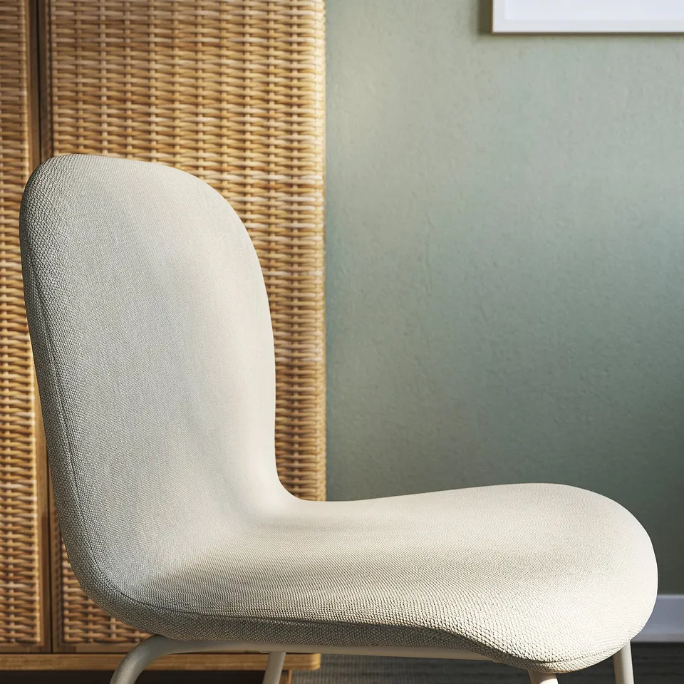 A modern, ergonomic chair with a high backrest and white upholstery, positioned against a woven screen and green wall.
