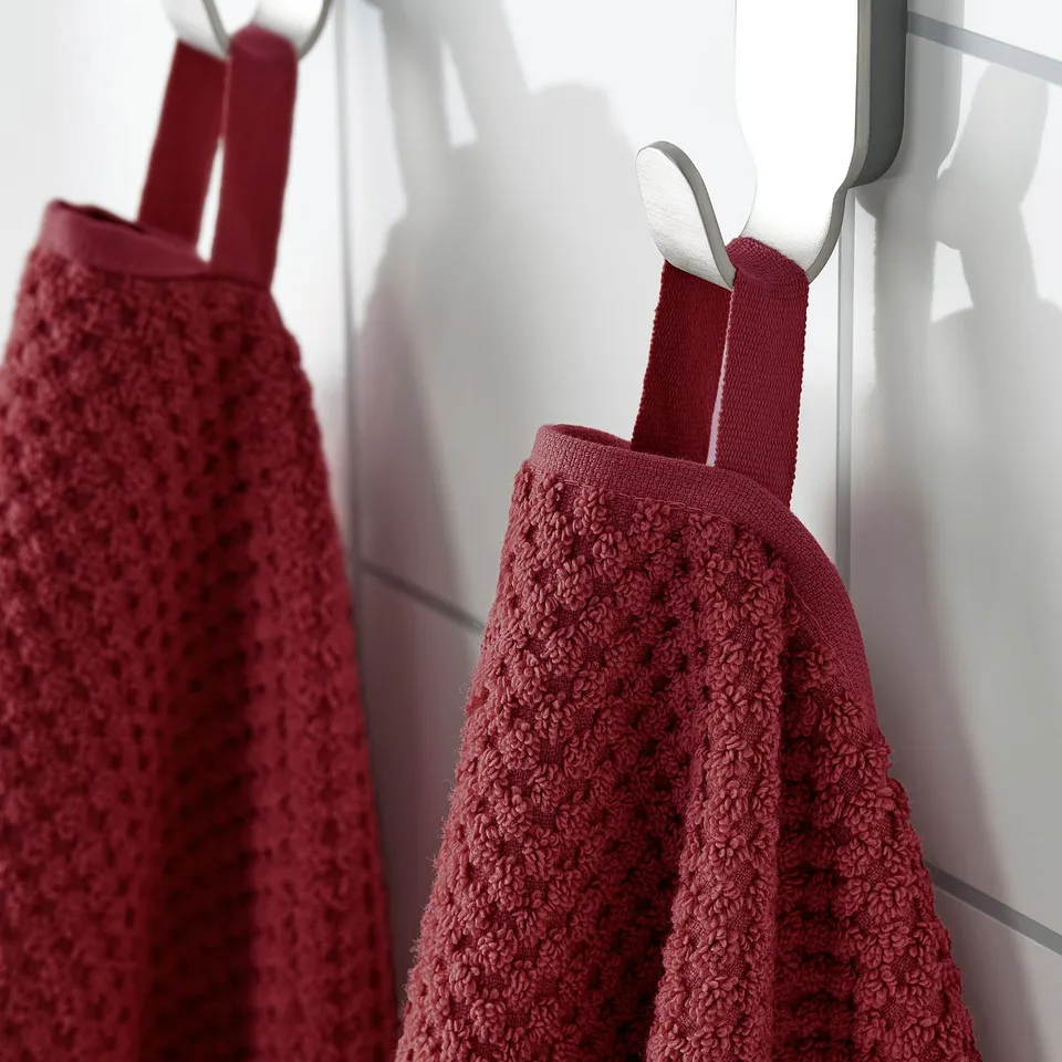 Two plush red towels hang neatly on white hooks, showcasing their soft, textured fabric designed for absorbency and durability.