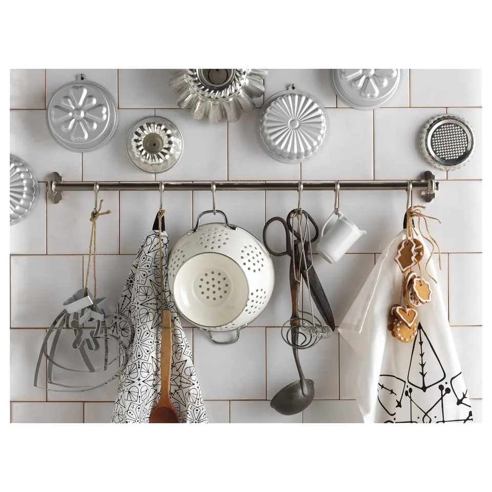 Kitchen wall with various metal utensils and hanging bakeware, steel hooks.