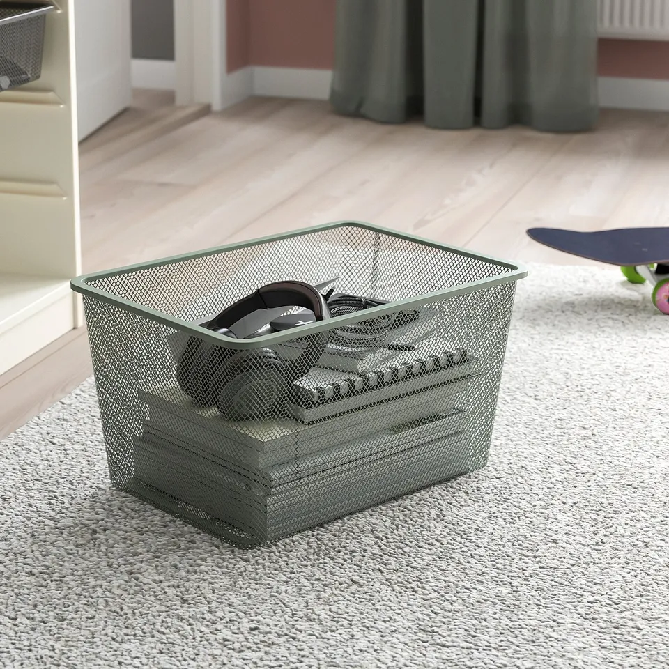 Mesh storage basket on floor with headphones and cables. Part of TROFAST series for organising items. Ideal for teens to keep things tidy.