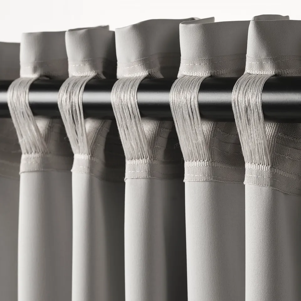 Close-up of curtains with pleated tops and hooks. These MAJGULL room-darkening curtains block light and provide privacy.