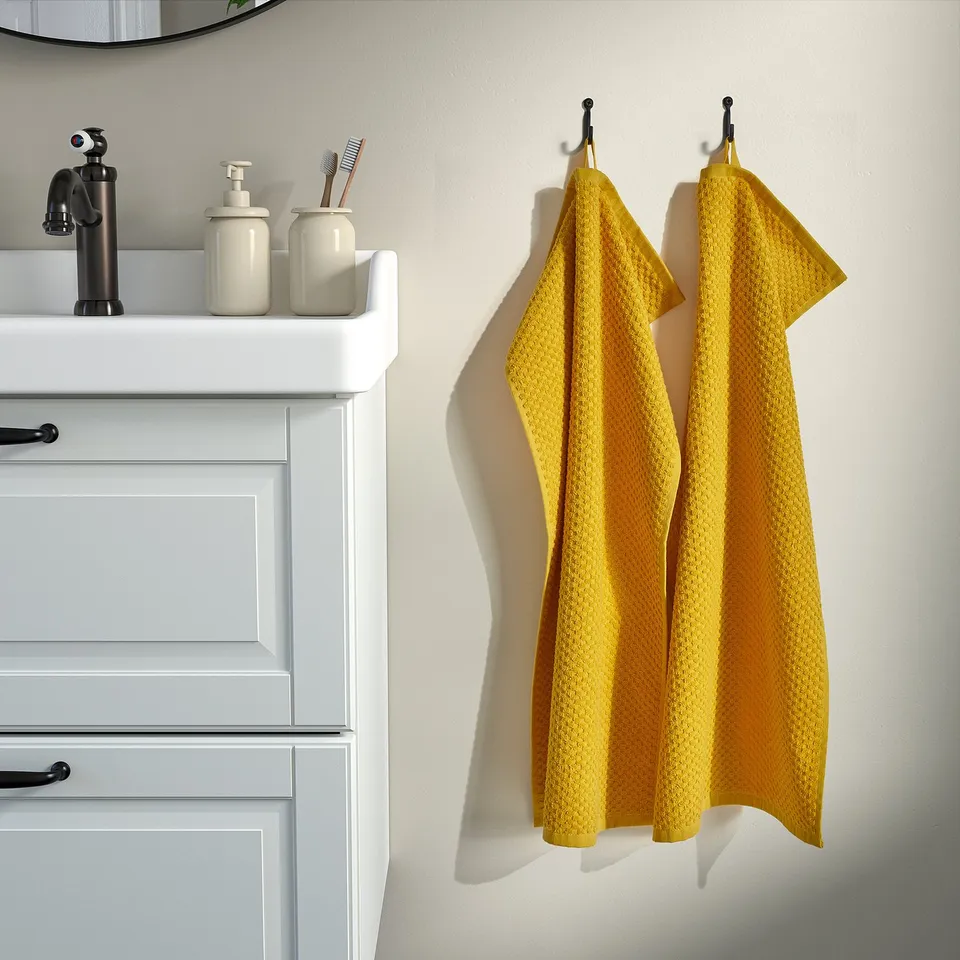 Yellow GULVIAL towels hang right of white vanity with black tap.