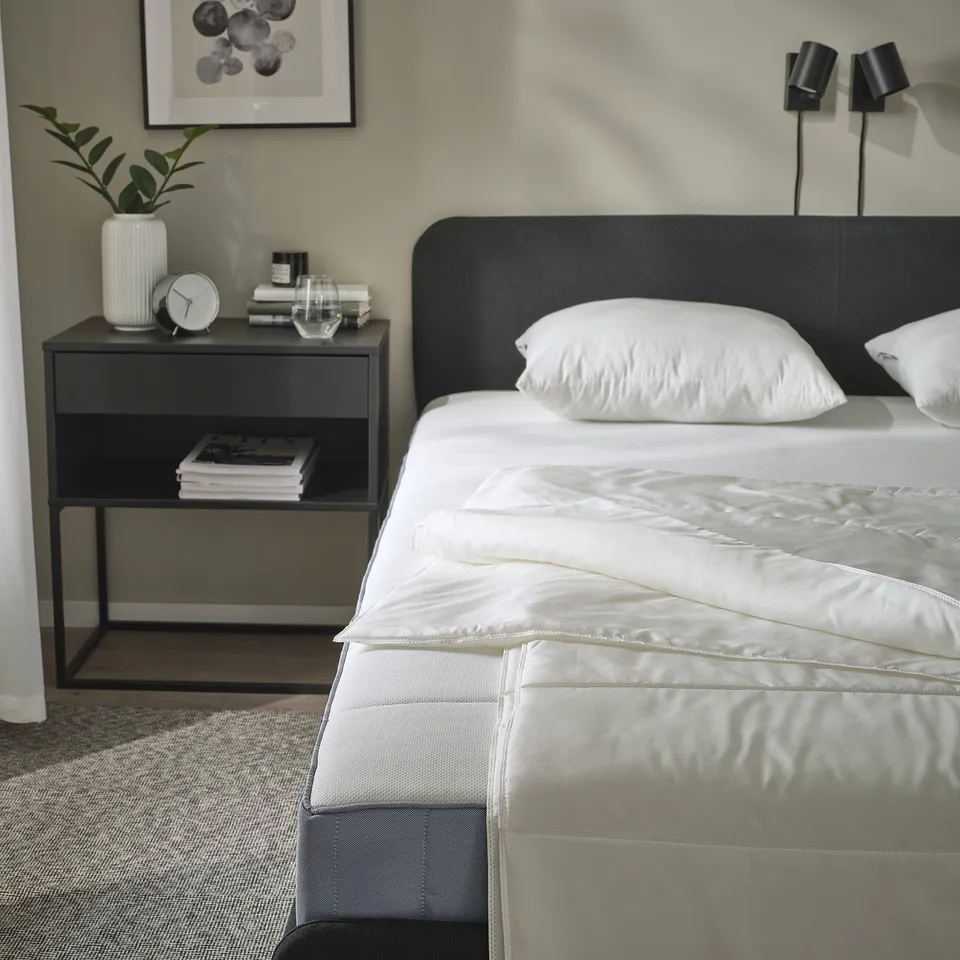 Bedroom with SANDGRÄSMAL duvet, bedside table with clock and books.