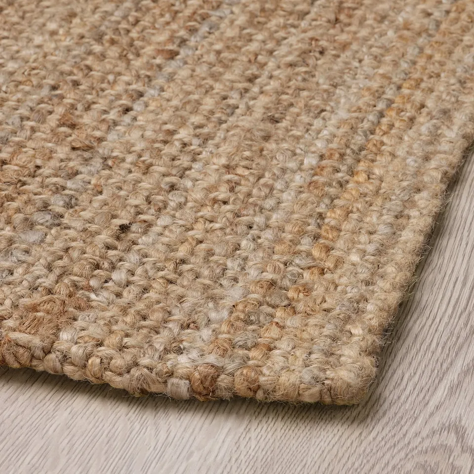 Natural jute rug, finely woven, laying on wooden floor. Dense, textured fibres create a soft, earthy look.