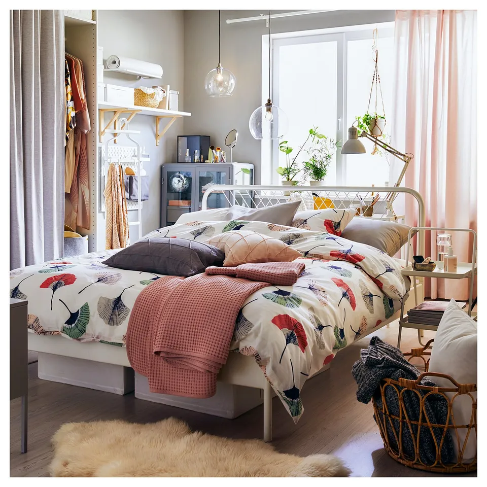 Bedroom with white metal bed, floral bedding, hanging light, basket, fur rug, and clothes rack.