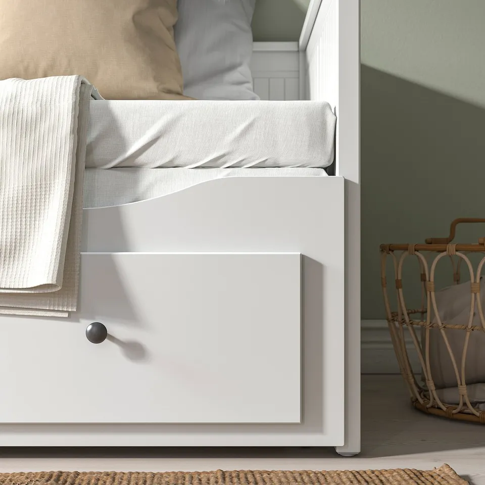 White daybed with open drawer, part of the HEMNES series. Pillows and blankets on top, basket beside it. Green wall in the background.