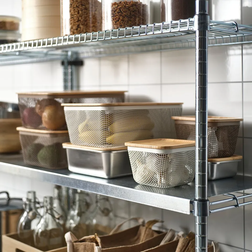 Metal shelf with mesh food storage baskets and lids. Lidless baskets hold produce, while stacked ones save space. Lower shelf has jars and cloth bags.