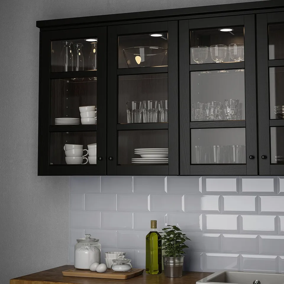 Wooden cabinets with black lights showcase white dishes. Grey counter holds plant and jars.