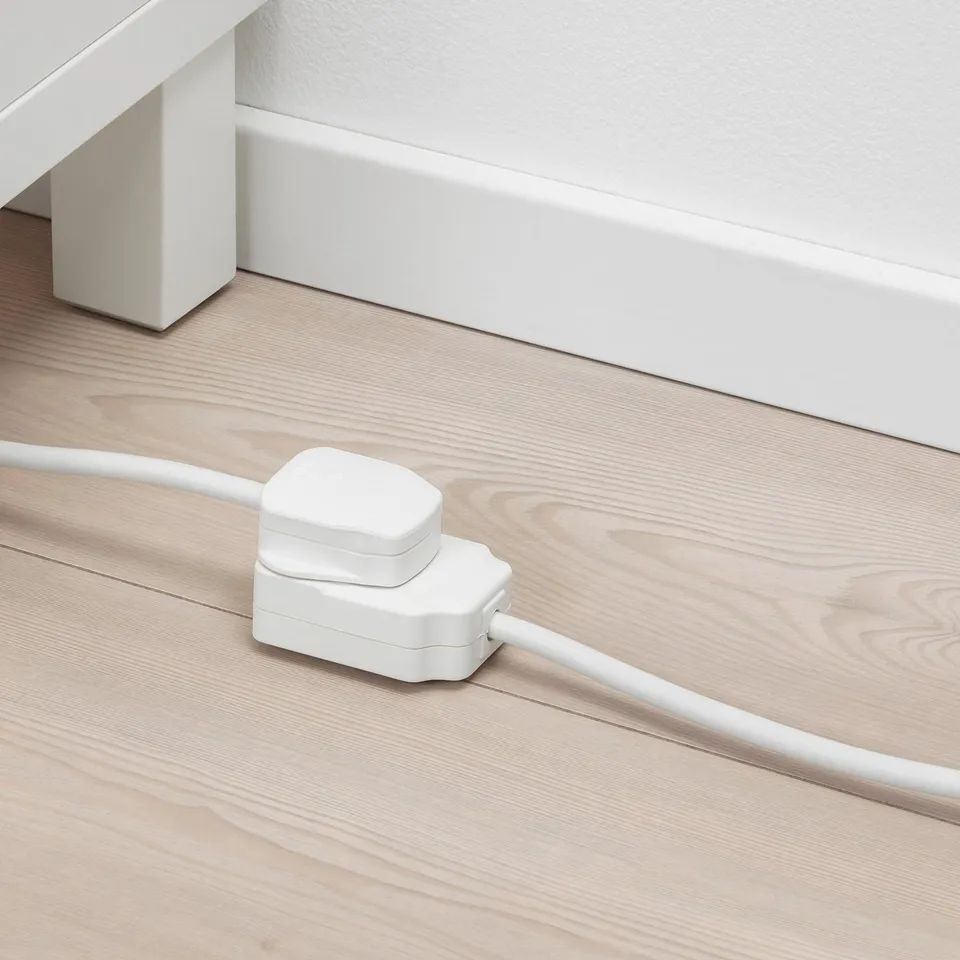 White extension cord on wooden floor, plugged in, providing power where needed.
