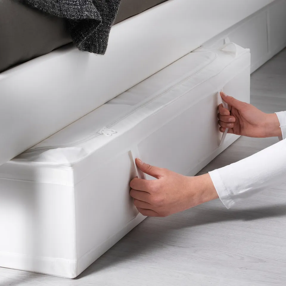 Person slides a white SKUBB storage case under a bed, featuring handles for easy access and ventilation for air circulation.