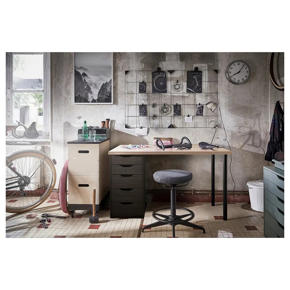 Industrial-style office setup with LAGKAPTEN desk, black stool, wall clock, bike, and decorative items.