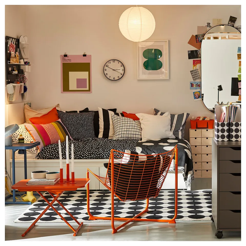 Bright living space with a black dotted rug and orange accents, featuring a cosy bed area, colourful pillows, and modern furniture.