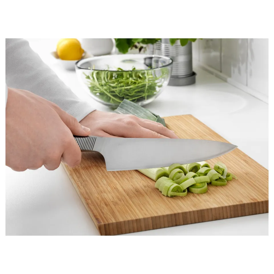 Person slicing green vegetables on a wooden cutting board using a silver knife.