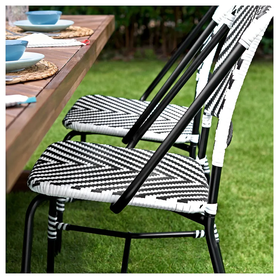 Black and white woven outdoor chairs, in a garden setting with a wooden table.