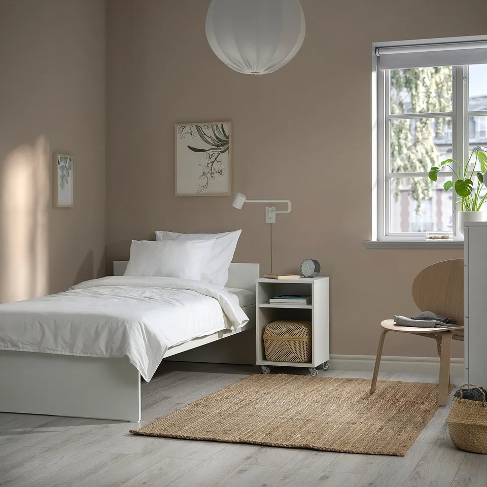 Bedroom with minimalist VIHALS bed, white linens, wooden chair, and artwork. Bed positioned against wall, under window.