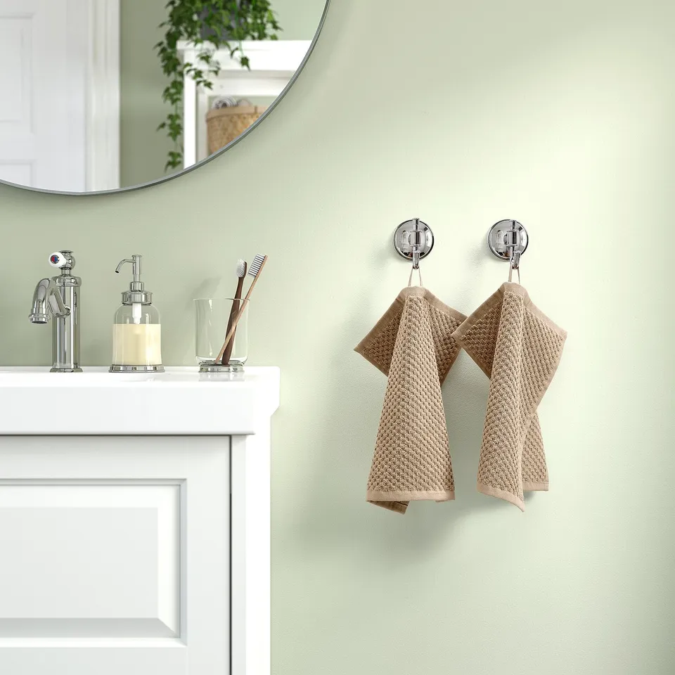 Modern bathroom with white sink, green wall, chrome fixtures. Two beige GULVIAL towels hang on wall hooks, soap dispenser, toothbrushes, mirror above.