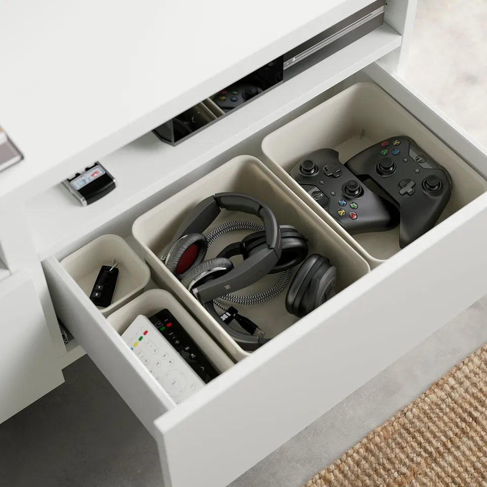 Drawer with gaming controllers, headphones, and remotes. Two black controllers shown.