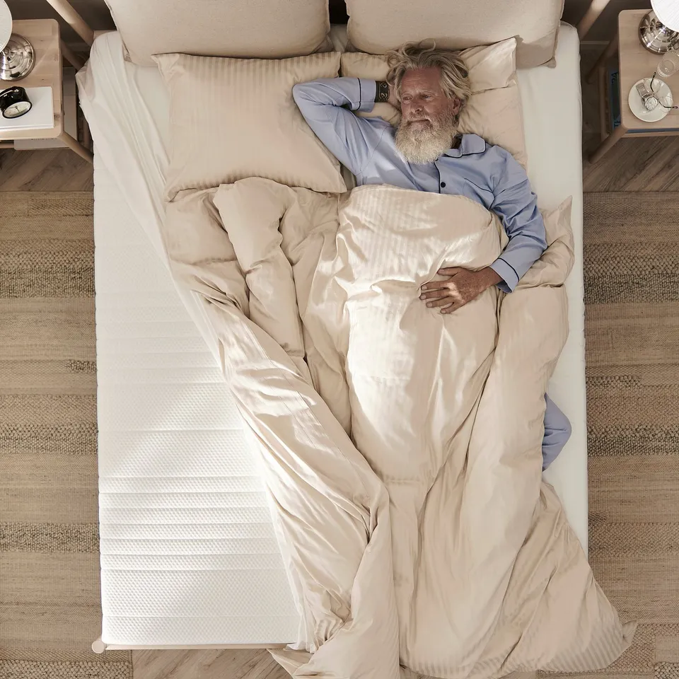 Top view of a person sleeping on a white ÅNNELAND mattress in blue pyjamas.
