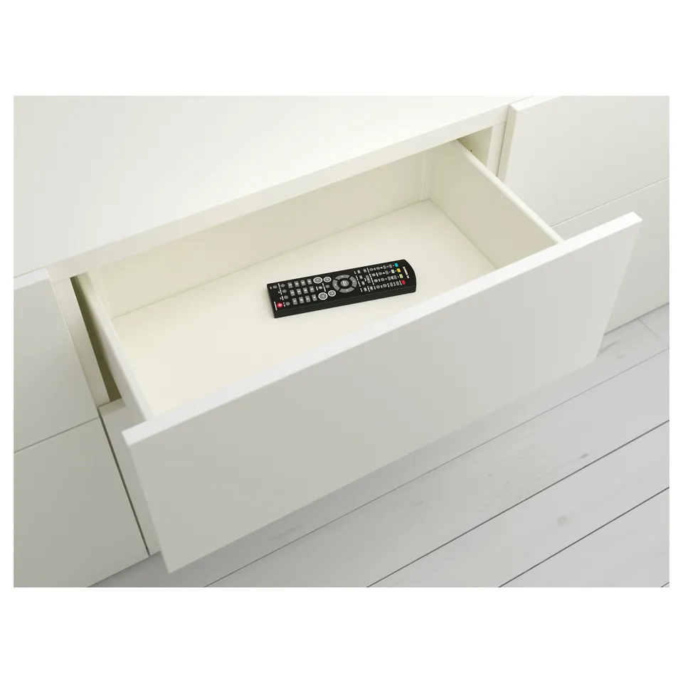 Open drawer of white BESTÅ unit with remote control inside.