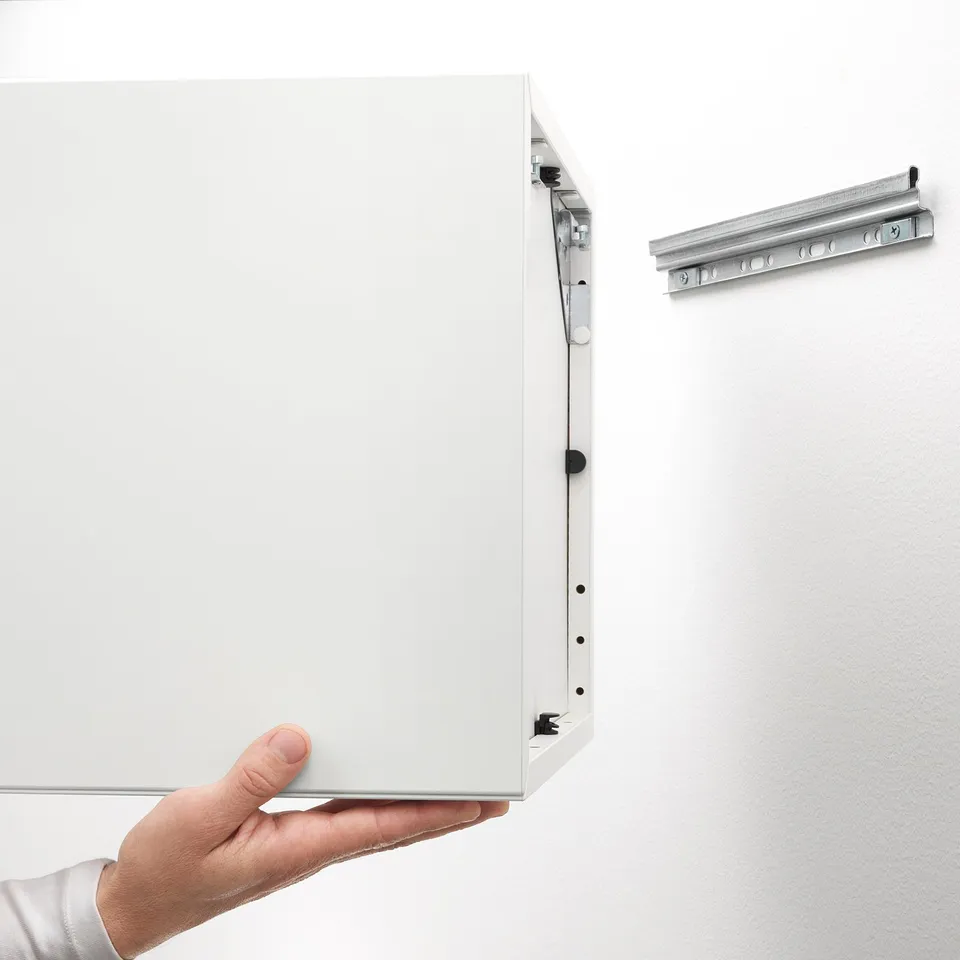 Hand holding open white cabinet showcasing hidden drawer mechanism. Wall-mounted storage solution with integrated suspension rails.