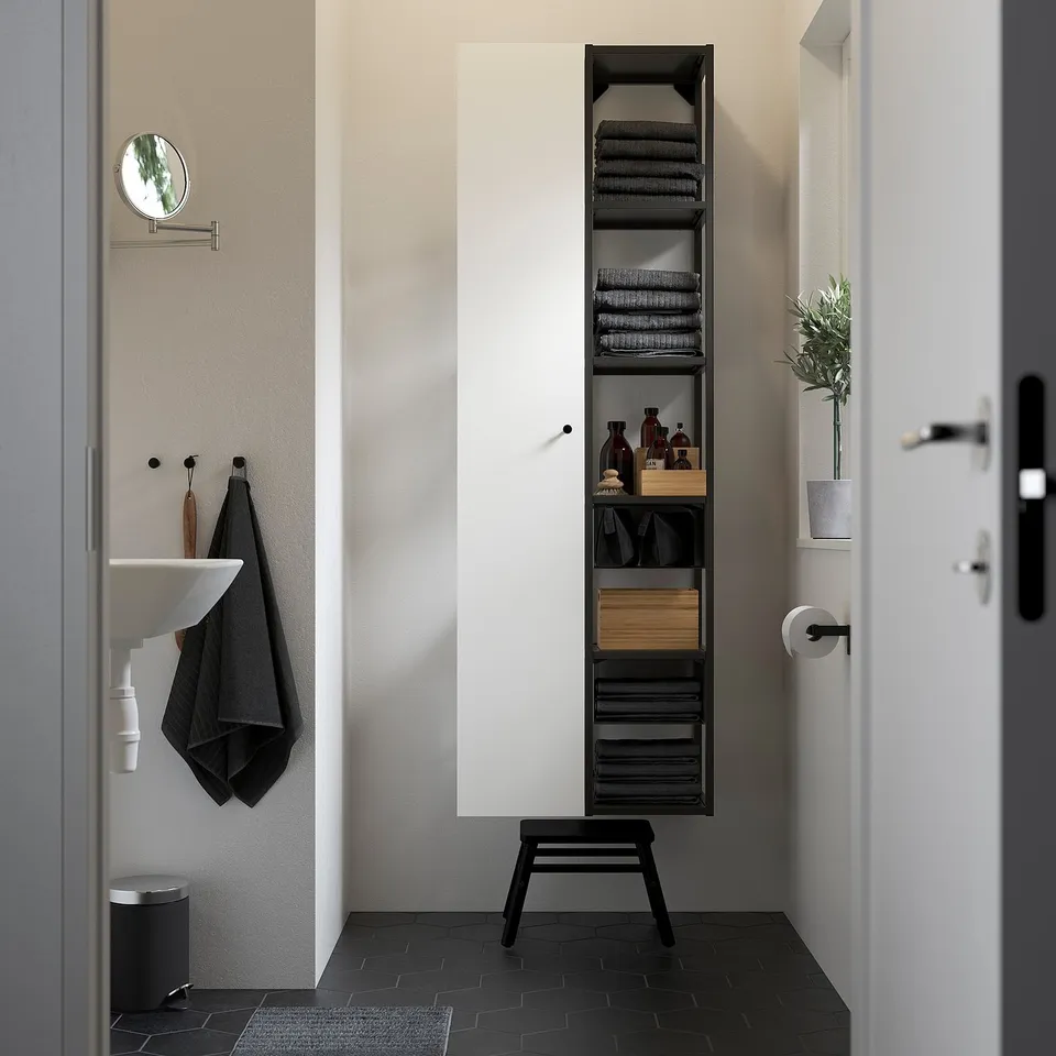 Modern bathroom with tall black ENHET shelving unit, white door cabinet, sink, mirror, and plant. Vertical storage.