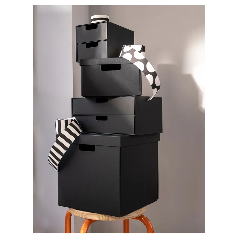 Four black FJÄDERHARV boxes on orange stool, wrapped with black-and-white ribbons.