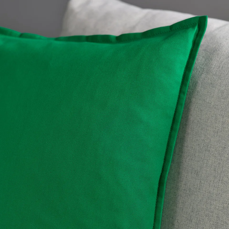 A close-up of a green cushion cover showcasing its smooth, soft texture and neat stitching.
