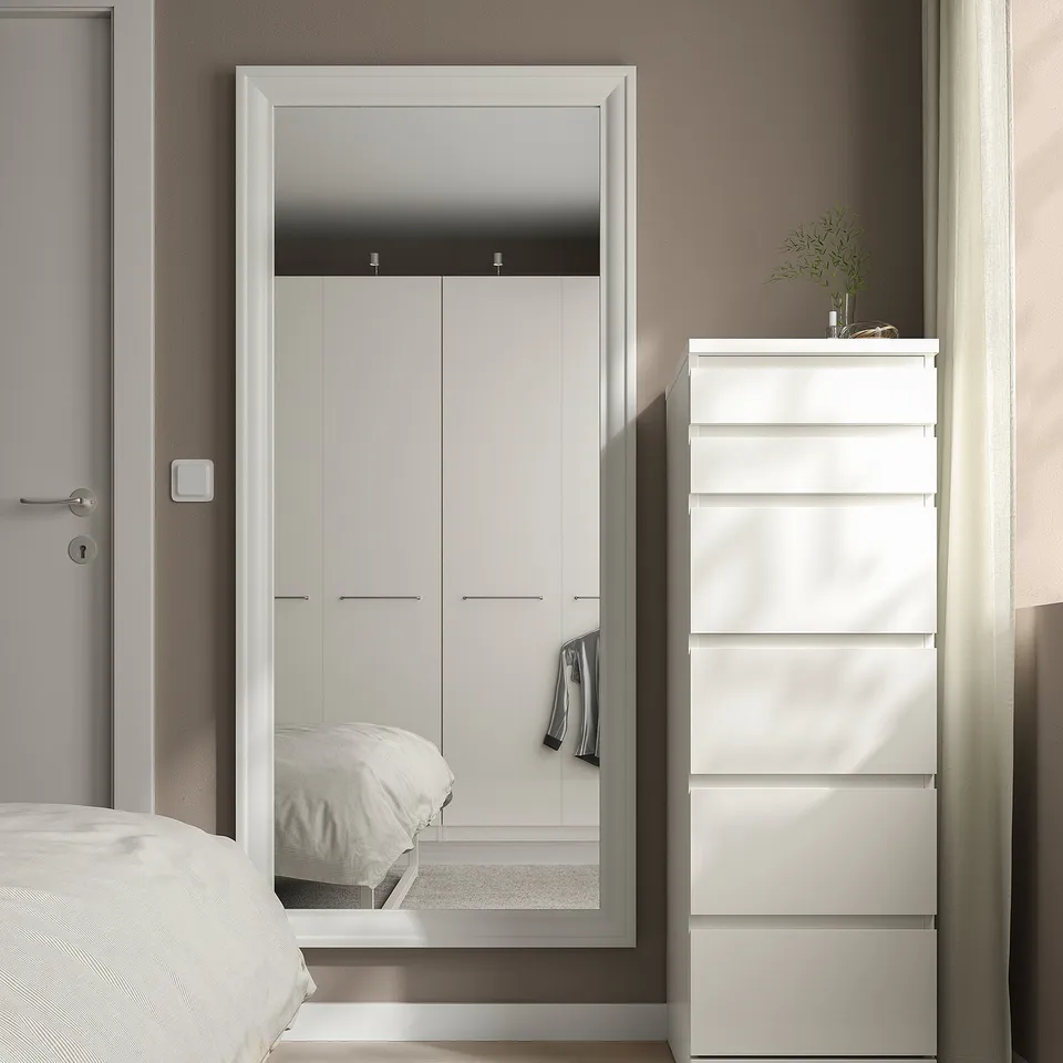 Modern bedroom with TOFTBYN mirror reflecting bed & wardrobe, enhancing minimalist style.