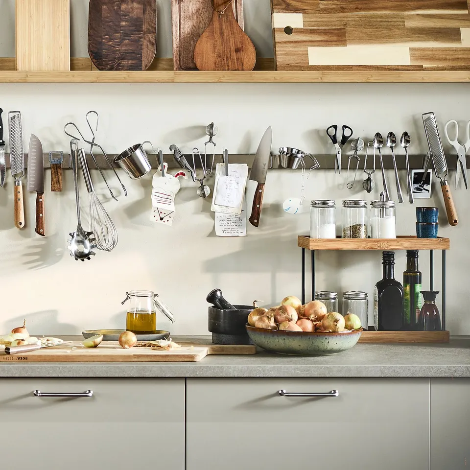 Well-organized kitchen with hanging tools, a cutting board, and a multi-level bamboo organiser for spices and bottles.