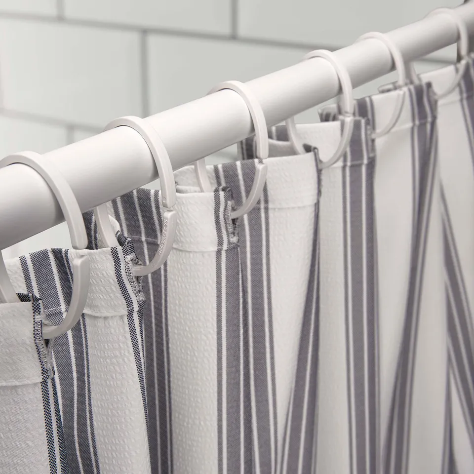 White striped shower curtain hanging on metal rod with plastic hooks.