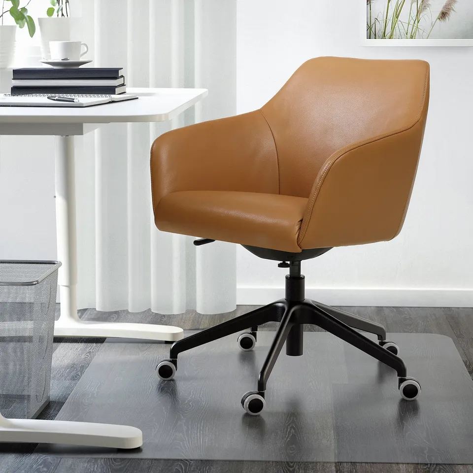 Brown leather TOSSBERG office chair, swivel, padded, high back, casters. Fits under white desk in minimalist home office.