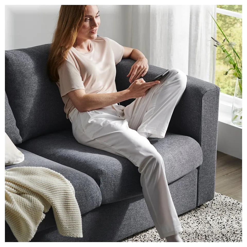 Person relaxes on grey VIMLE sofa, light outfit, cosy living room setting.