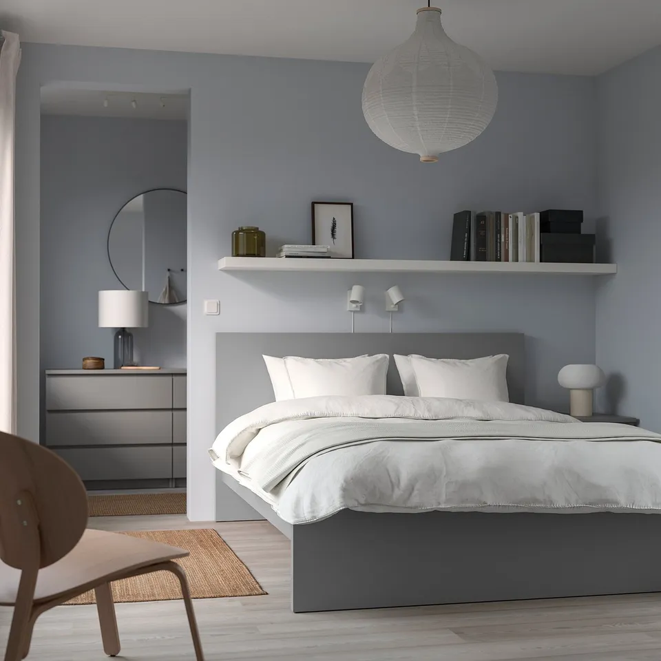 Minimalist grey MALM bed with white linens, wooden chair, pendant lamp, and bookshelf in modern bedroom.