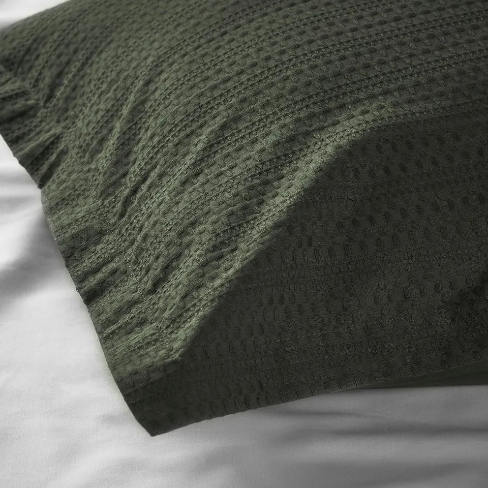 Dark green duvet cover with waffle texture, showcasing soft, woven cotton fabric. Folded neatly, highlighting its quality and comfortable touch.