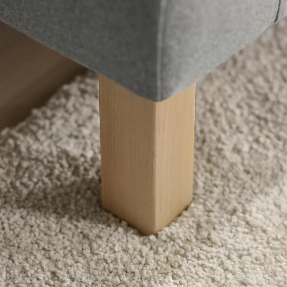 Close-up of modern footstools sturdy wooden leg. Light beige carpet visible underneath.