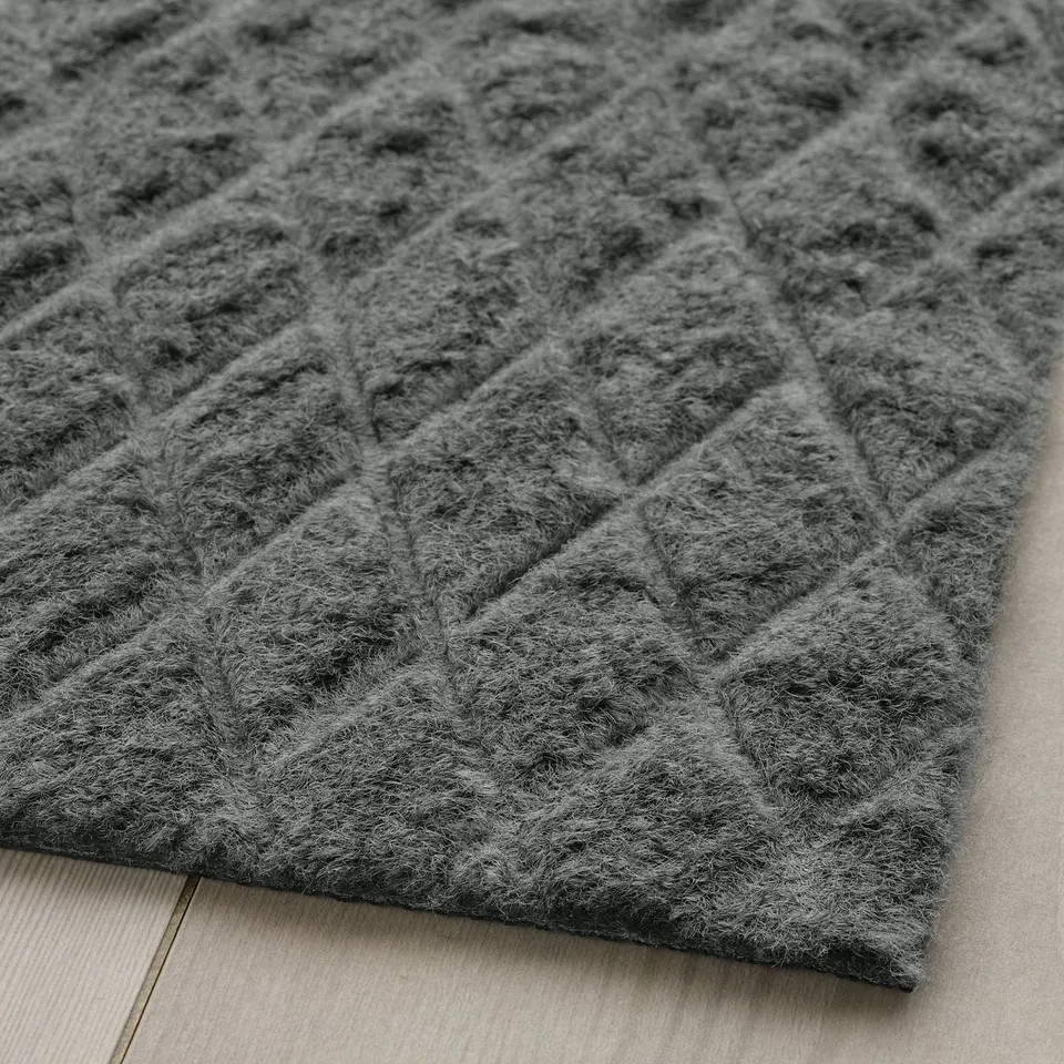 Grey textured doormat with diamond pattern on wooden floor.