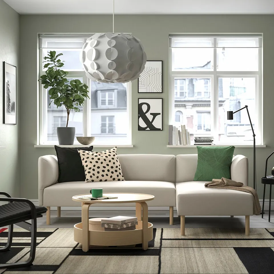 Modern living room with LILLEHEM sofa, green pillows, coffee table, black-white rug, large windows, unique lighting.