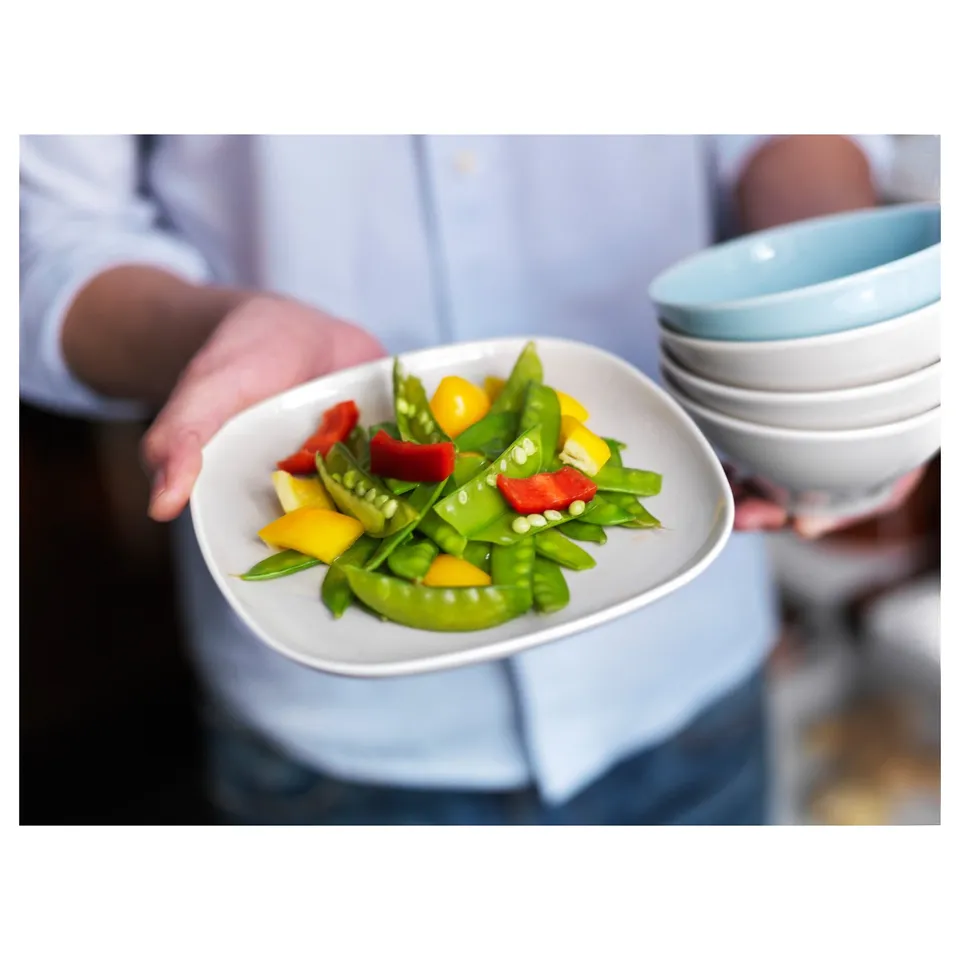 A person holding a square white VÄRDERA plate, filled with colourful vegetables. Soft, rounded edges; durable feldspar porcelain.
