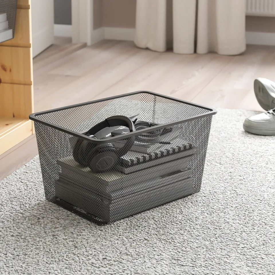 Metal mesh basket holds headphones, part of TROFAST storage series, ideal for organising electronics.