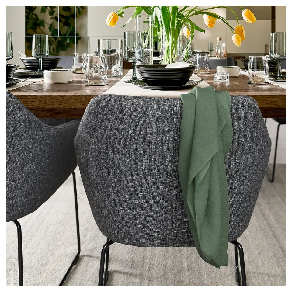 Elegant dining setup with modern wooden table, grey chairs, yellow flowers, plates, and glasses.